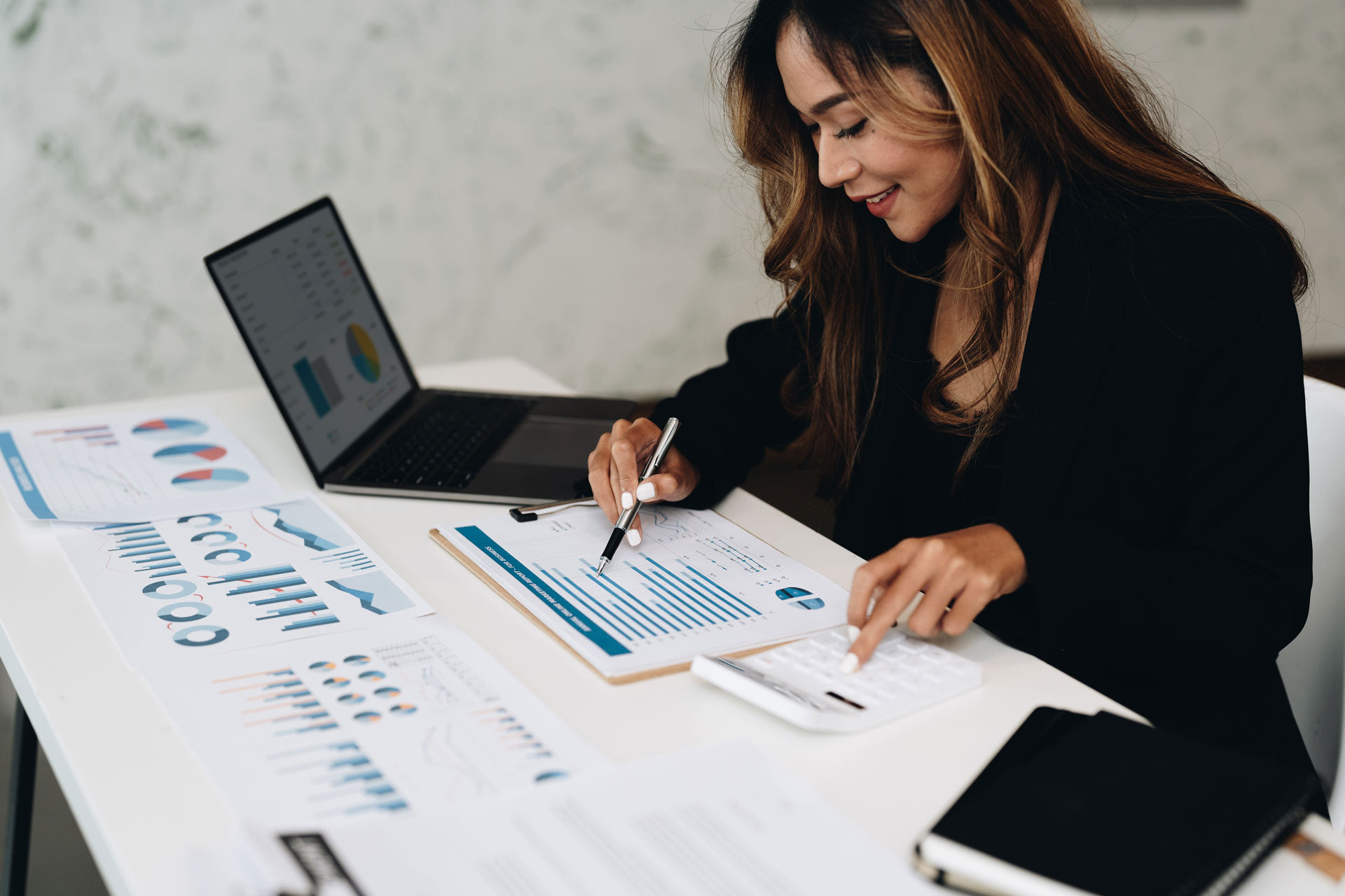 Businesswoman reviewing data reports and charts while using a laptop and calculator.